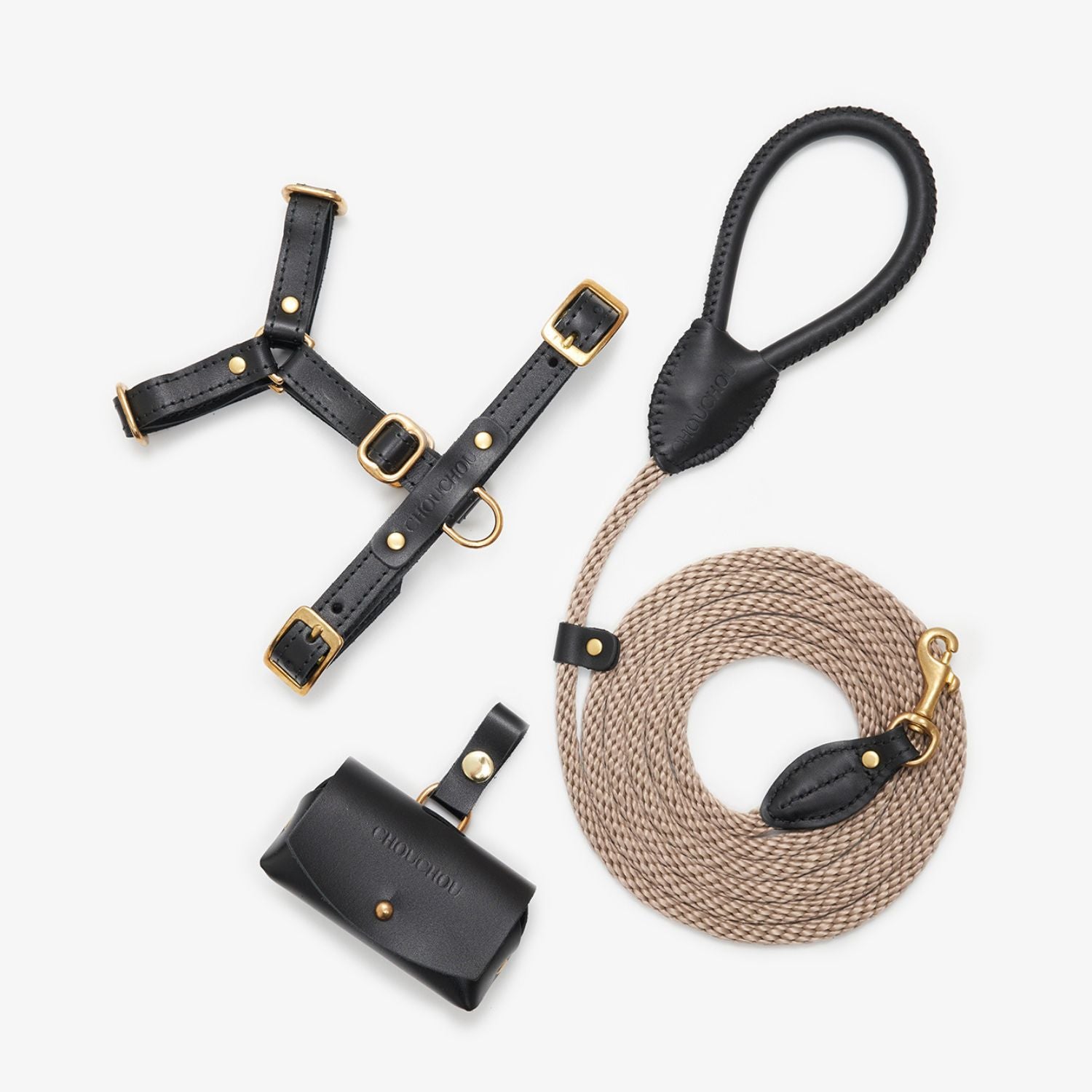 Minimalist flatlay of the black leather dog walking set by CacheMio & CHOUCHOÚ, featuring a harness, rope leash, and poop bag holder.