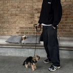 Person walking a small Yorkshire Terrier wearing the CacheMio & CHOUCHOÚ black leather harness and shock-absorbing rope leash.