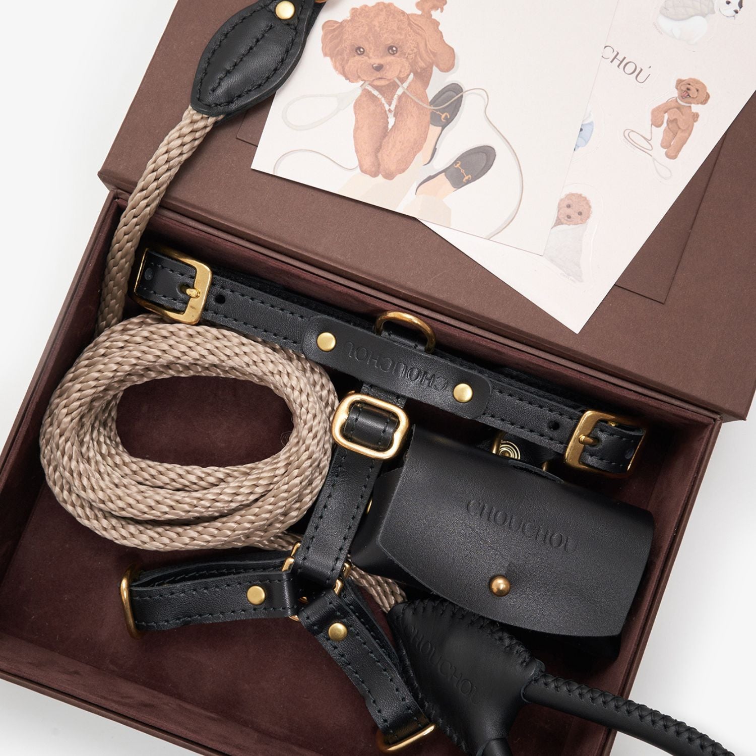 Close-up of the black premium leather dog harness, rope leash, and waste bag holder by CacheMio & CHOUCHOÚ inside the signature brown gift box.