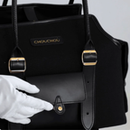A white-gloved hand delicately opens the front smooth leather compartment, highlighting the meticulous craftsmanship and secure snap closure of the dark carrier.
