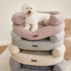 A playful white Bichon Frise stands proudly atop a vertical stack of premium orthopedic dog beds, showcasing the sophisticated pastel and neutral color palette of the collection.