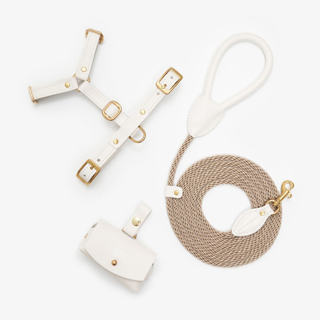 Minimalist flatlay of the complete milk white dog walking set by CacheMio & CHOUCHOÚ, featuring a leather harness, rope leash, and dispenser.