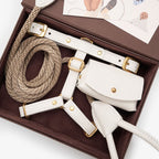 Close-up of the milk white premium leather dog harness, rope leash, and waste bag holder by CacheMio & CHOUCHOÚ inside the signature brown gift box.