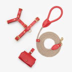 Minimalist flatlay of the complete red dog walking set by CacheMio & CHOUCHOÚ, featuring a leather harness, shock-absorbing rope leash, and poop bag dispenser.
