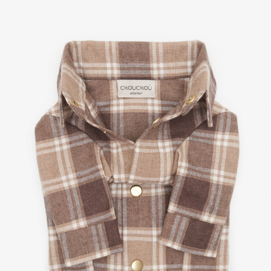 Extreme close-up of an unbuttoned brown plaid dog shirt collar, revealing the CHOUCHOÚ atelier fabric tag and metallic snap buttons.