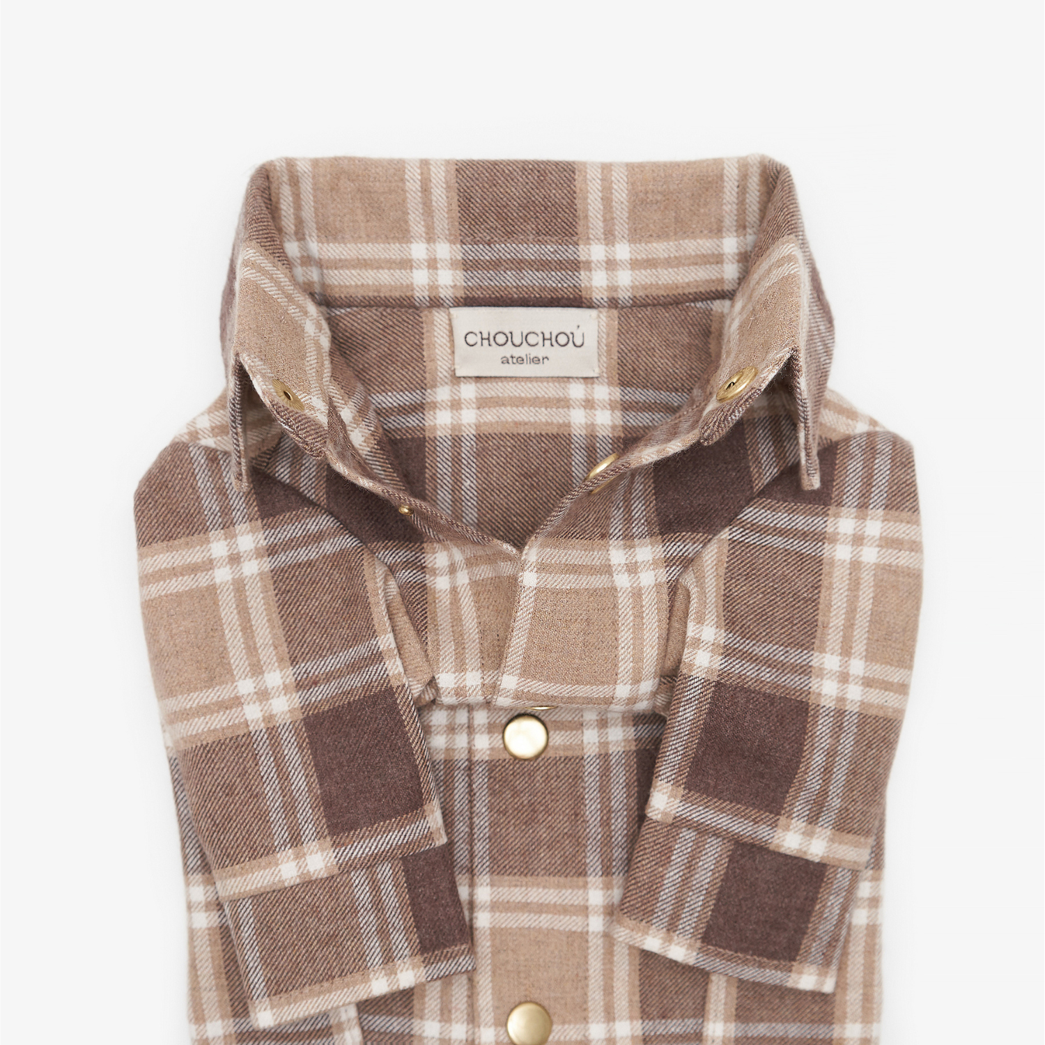 Extreme close-up of an unbuttoned brown plaid dog shirt collar, revealing the CHOUCHOÚ atelier fabric tag and metallic snap buttons.