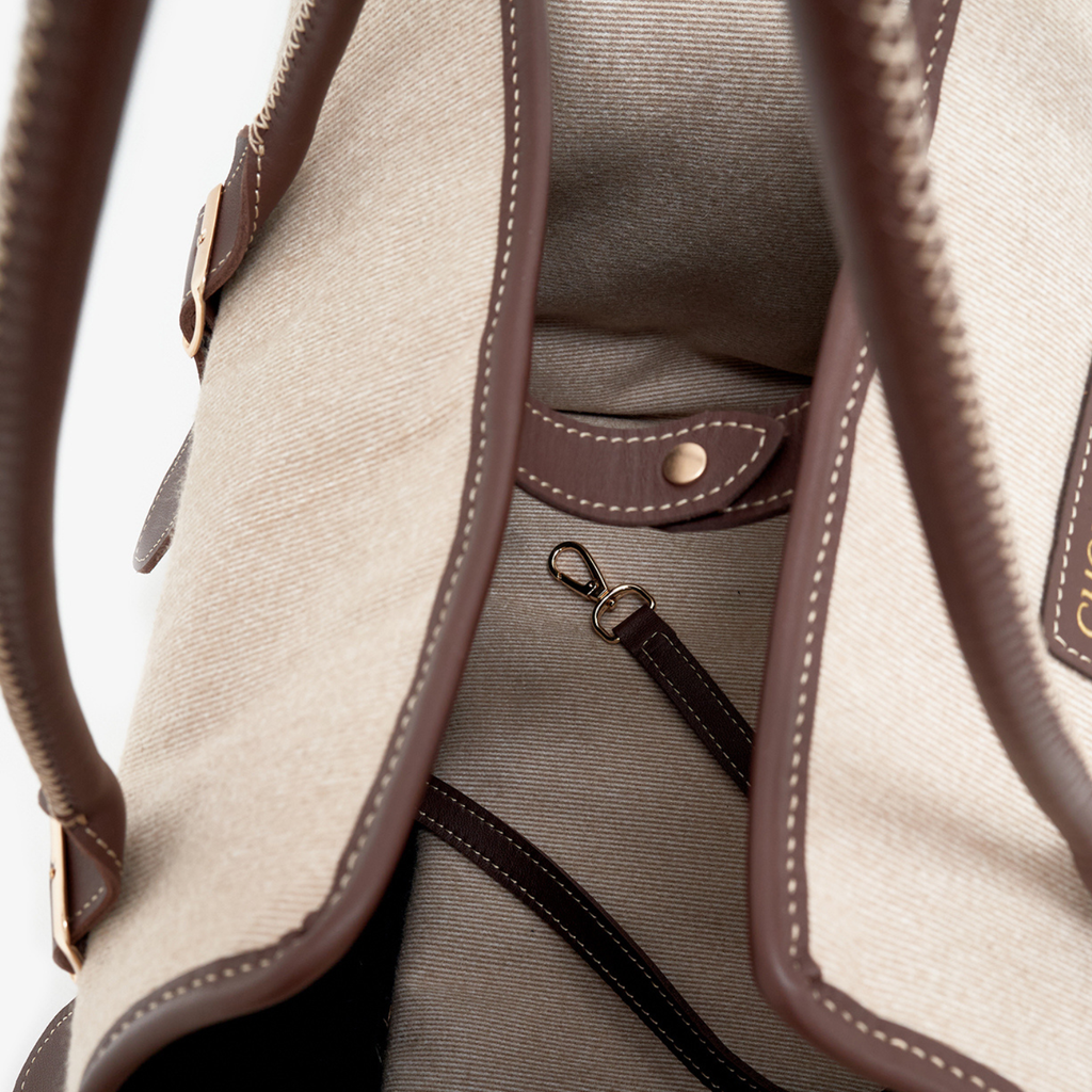 Meticulous leather binding outlines the opening of the tactile canvas pet tote, framing the internal security hardware designed for safe city mobility.