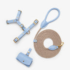 Minimalist flatlay of the CHOUCHOÚ light blue dog walking set, featuring a leather harness, rope leash, and poop bag dispenser.