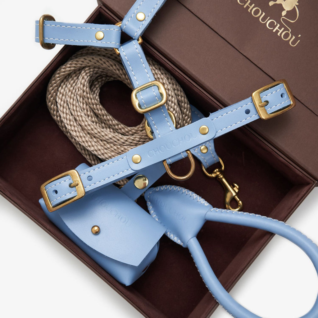 Light blue premium Italian leather dog harness, rope leash, and bag holder by CHOUCHOÚ inside a brown magnetic gift box.