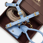 Light blue premium Italian leather dog harness, rope leash, and bag holder by CHOUCHOÚ inside a brown magnetic gift box.