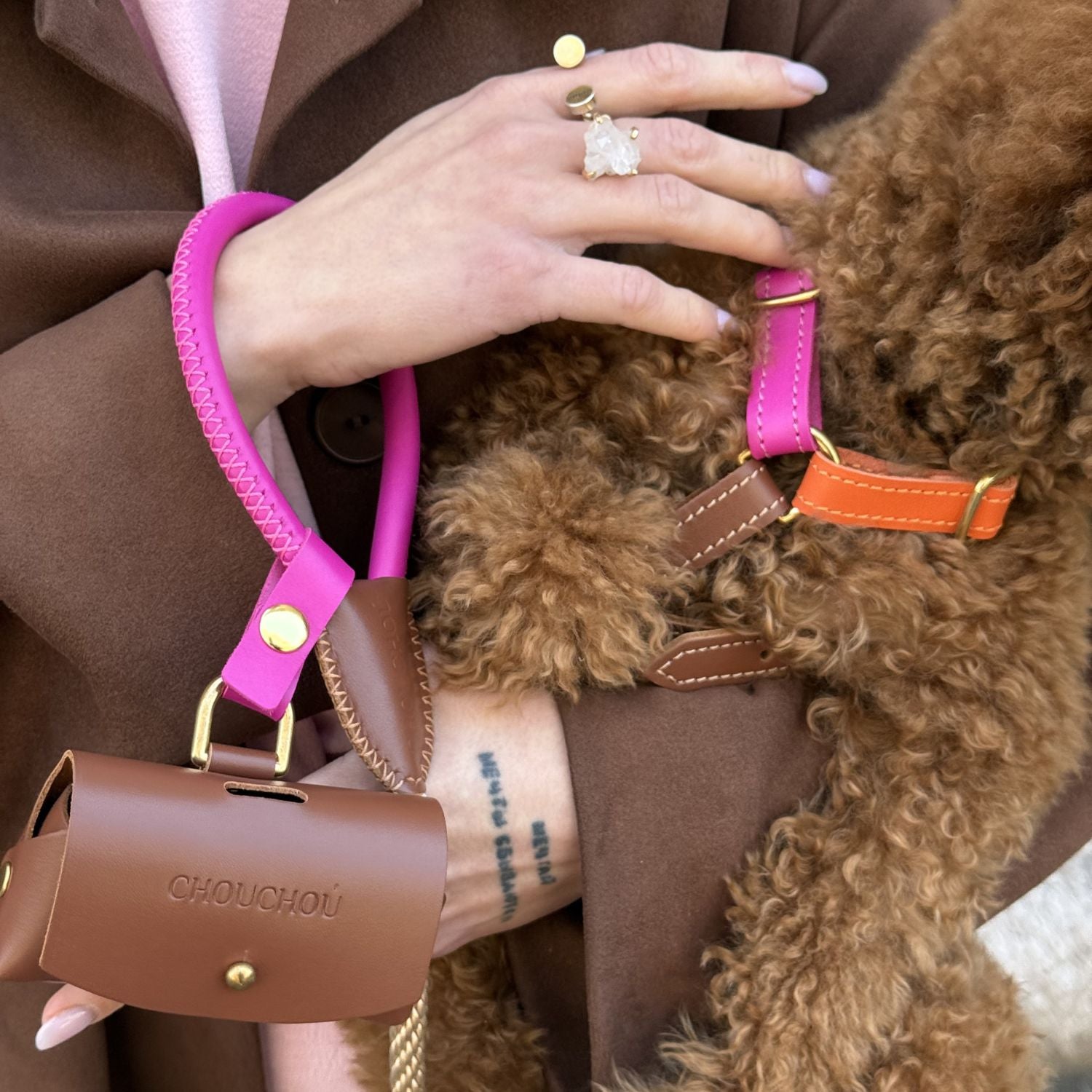 Close-up shot of a pet owner holding a vibrant pink leather leash loop and a discreet brown poop bag dispenser during a city walk.