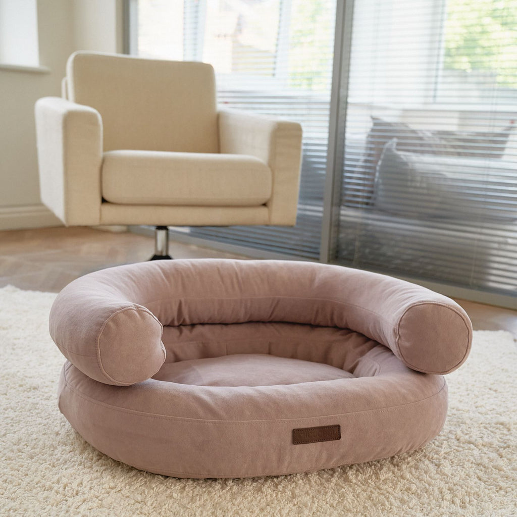 The pink Marshmallow dog bed by CHOUCHOÚ styled as a functional design object in a modern living room with a beige armchair and natural light.