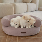 Three adorable white Pomeranian puppies snuggling together inside the spacious pink Marshmallow orthopedic dog bed by CHOUCHOÚ on a wooden floor.